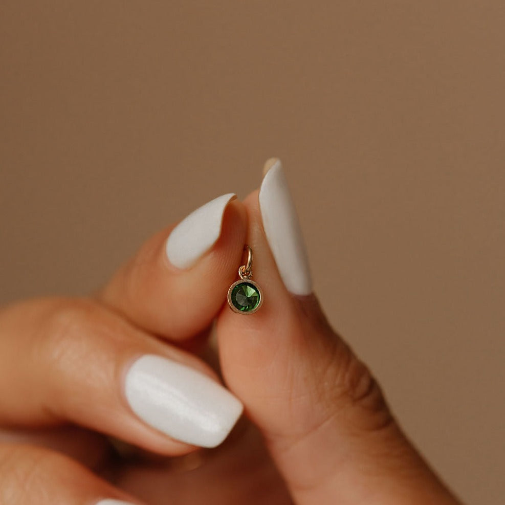 a woman is holding a tiny birthstone charm made in canada