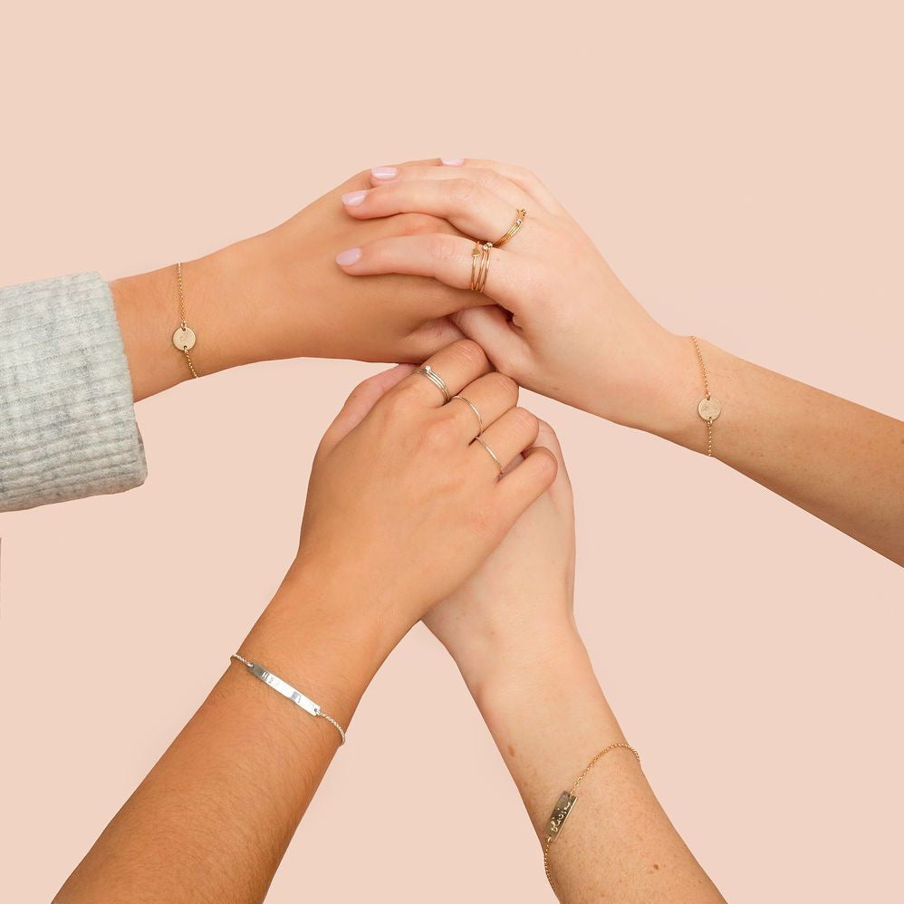 Friends holding hands wearing custom handmade initial bracelets and custom message handmade bar bracelets  