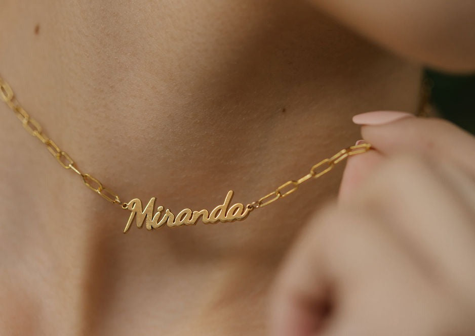 a woman is holding necklace made with name and link chain in gold