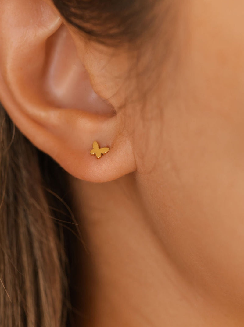 A woman is wearing butterfly stud earrings in gold.