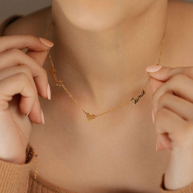 a woman holding a name necklace with heart pendants gold