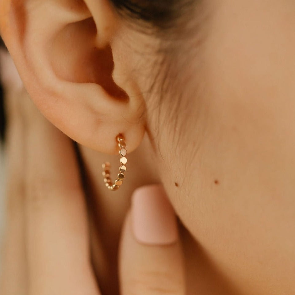 a woman is wearing gold flat bead huggie