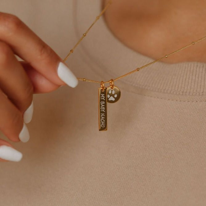 A woman is holding the paw print coin pendant and name engraved bar jewelry. 