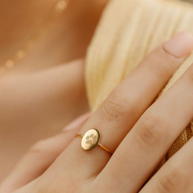 a woman is wearing an oval paw print ring in gold