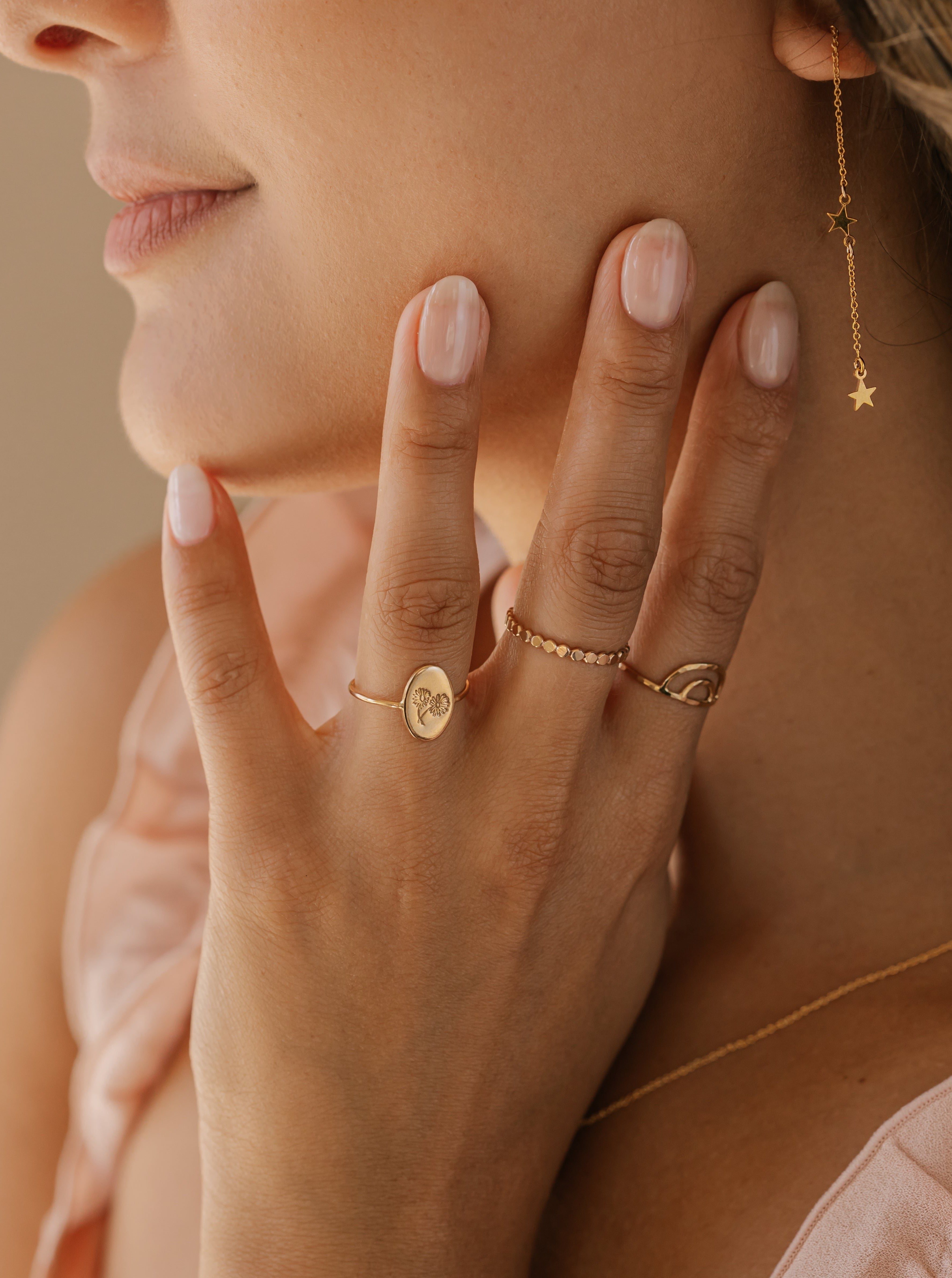 a woman is wearing a star threader earrings in gold and also wearing anti-tarnish stackable rings made in Canada.