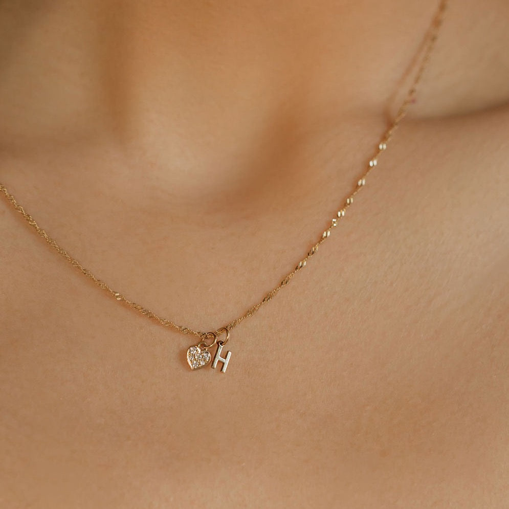 a woman is earring a diamond heart charm and initial H charm necklace made in Canada