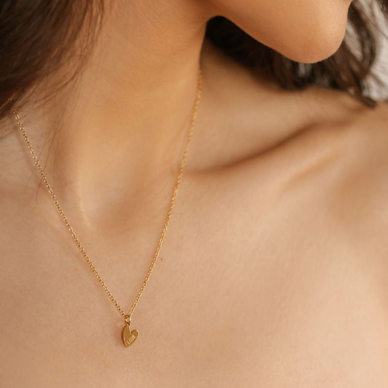 a woman is wearing a gold love engraved heart pendant necklace made in Canada