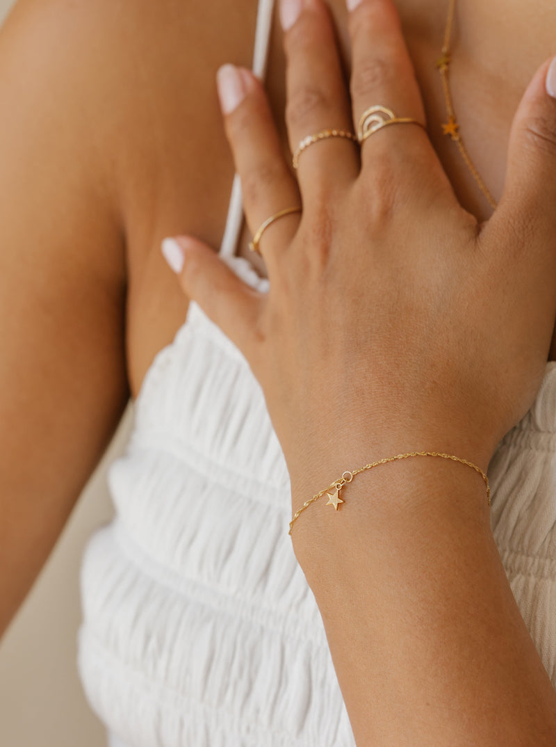 a woman is wearing a star bracelet in 14k solid gold. 
