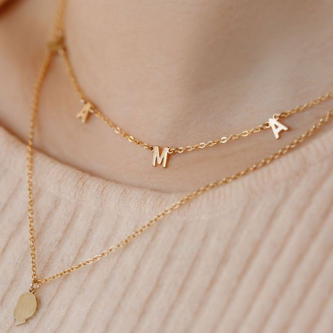 Close up image of layered necklaces, one is a gold kid silhouette necklace 18 inches and the short 16 inch necklace is a gold necklace that spells out MAMA