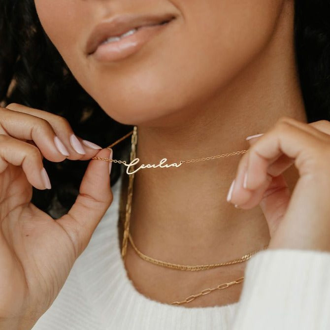 A woman is holding Cursive Name Necklace in gold
