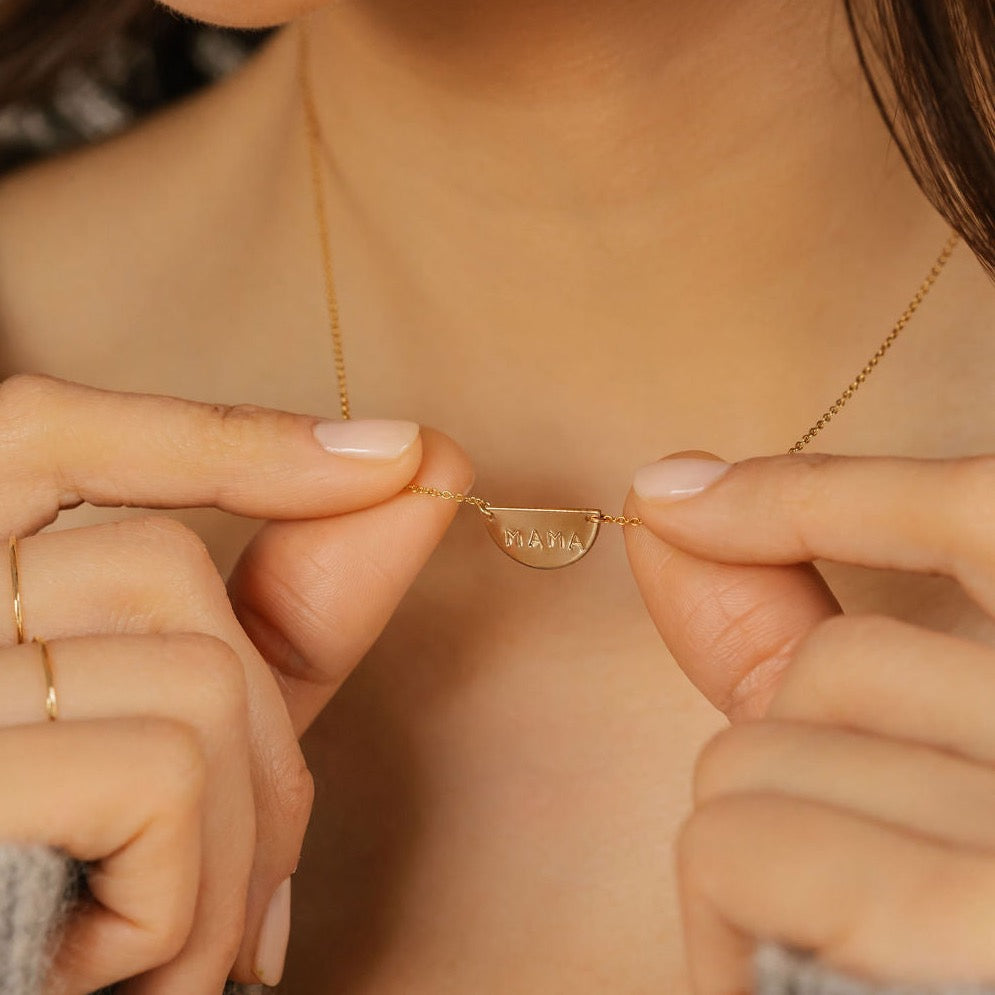 a woman is holding a gold filled mama initial half moon necklace in Canada