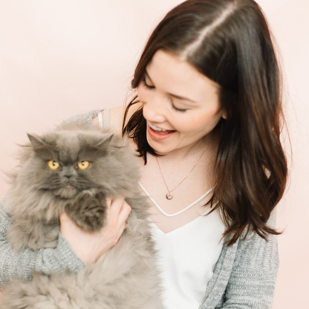 Woman laughing and holding cat wearing handmade custom paw print coin necklace sustainably made in Canada