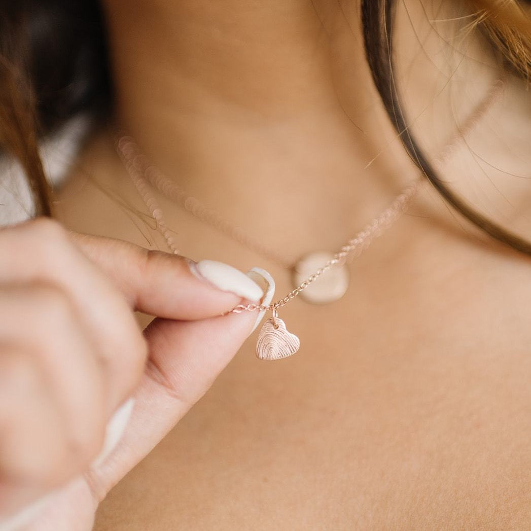 Woman showing actual fingerprint on custom handmade tiny heart fingerprint necklace in rose gold