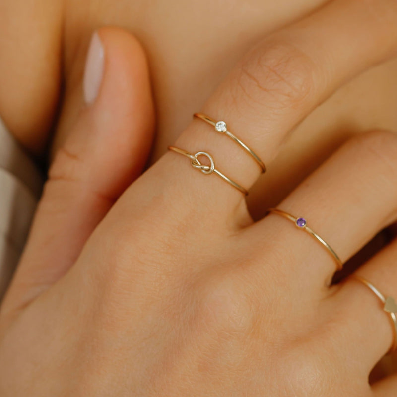 a woman is wearing minimal stackable birthstone and knot rings